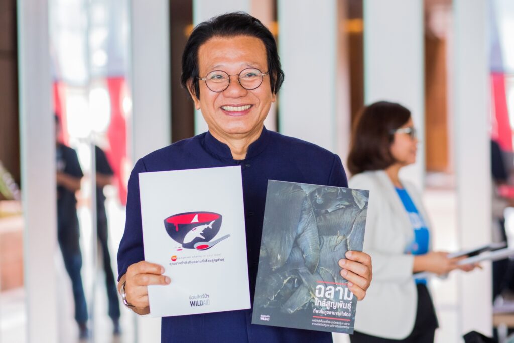 Dr. Tossaporn Serirak, a member of Thailand's Parliament, holds up two signs about a shark fin DNA study.